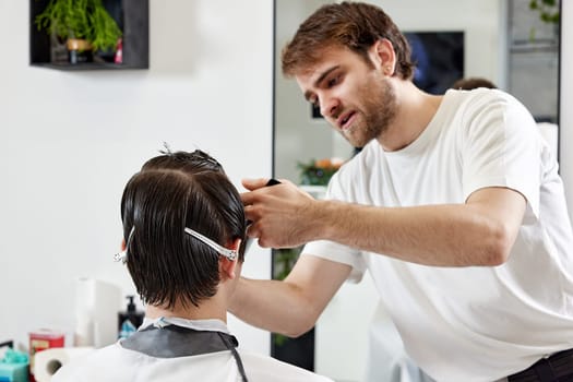 Professional barber during work with man client in barber shop.