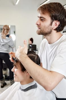 friendly barber combing young caucasian client man at barber shop.