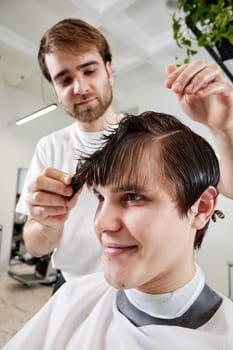 friendly barber combing young caucasian client man at barber shop.
