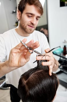 professional male hairstylist serving young caucasian client man at modern barber shop.