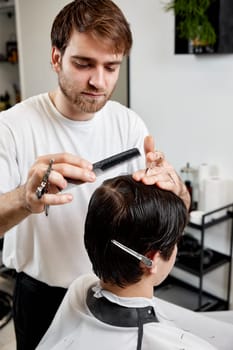 professional male hairstylist serving young caucasian client man at modern barber shop.