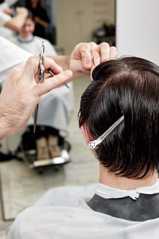 professional male hairstylist serving young caucasian client man at modern barber shop.