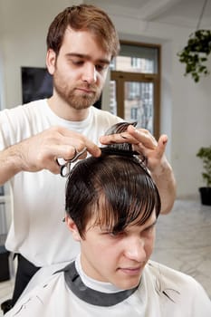 professional male hairstylist serving young caucasian client man at modern barber shop.