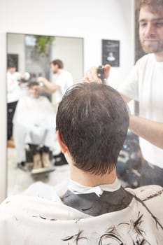 young caucasian man getting haircut by professional male hairstylist using comb and sprayer at barber shop.