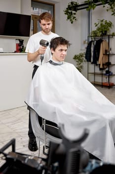 Professional hairdresser during work with man client with hair dryer in barber shop. Haircut in the barbershop.