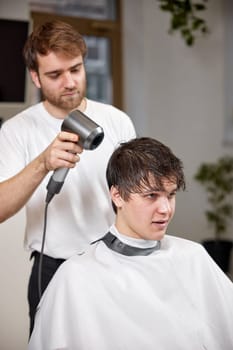 Professional hairdresser during work with man client with hair dryer in barber shop. Haircut in the barbershop.