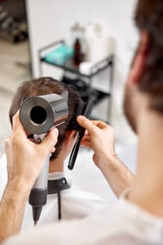 Professional hairdresser using hair dryer and hairbrush of his client in barber shop. Haircut in the barbershop.