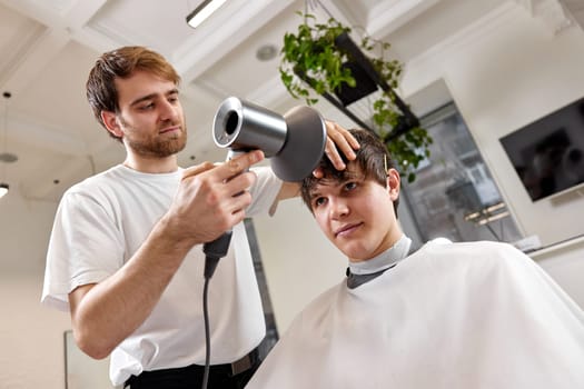 Professional hairdresser during work with man client with hair dryer in barber shop. Haircut in the barbershop.