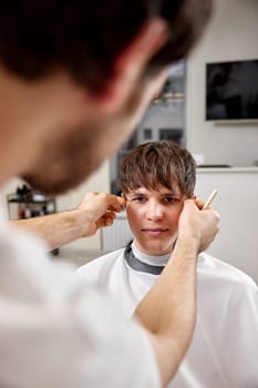 young caucasian man getting haircut by professional male hairstylist at barber shop.