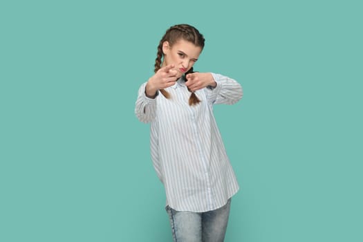 Portrait of positive optimistic flirting teenager girl with braids wearing striped shirt pointing fingers to camera, choosing you. Indoor studio shot isolated on green background.