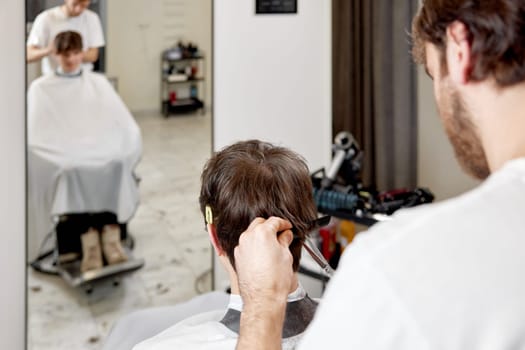 young caucasian man getting haircut by professional male hairstylist at barber shop.