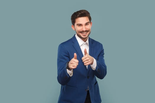 Portrait of satisfied delighted man standing showing thumbs up, recommend good service, approved gesture, looking smiling at camera, wearing Indoor studio shot isolated on light blue background.