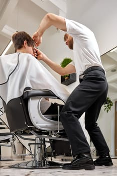 young caucasian man getting haircut by professional male hairstylist at barber shop.