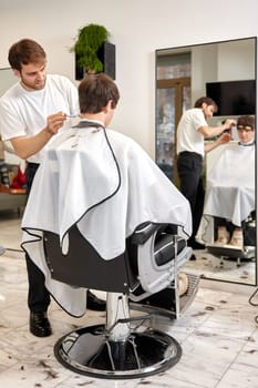 young caucasian man getting haircut by professional male hairstylist at barber shop.