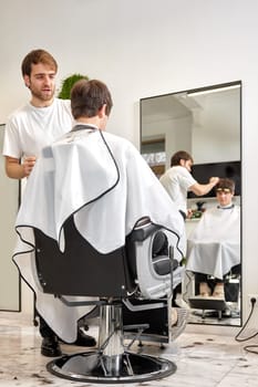 young caucasian man getting haircut by professional male hairstylist at barber shop.