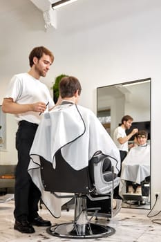 young caucasian man getting haircut by professional male hairstylist at barber shop.
