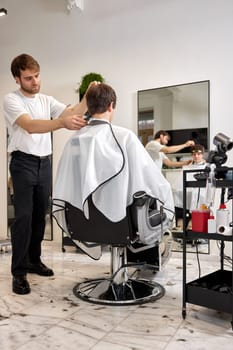 young caucasian man getting haircut by professional male hairstylist at barber shop.