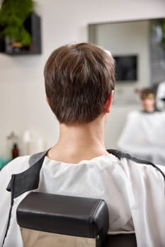young man looks at his reflection in the mirror while sitting in chair in barbershop