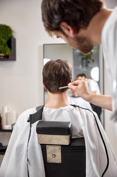 young caucasian man getting haircut by professional male hairstylist at barber shop.