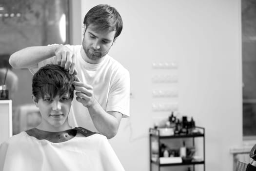 young caucasian man getting haircut by professional male hairstylist at barber shop. black and white