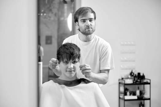 young caucasian man getting haircut by professional male hairstylist at barber shop. black and white