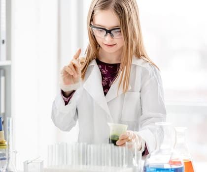 Smart girl doing scientific chemistry experiment wearing protection glasses and holding bottle with green liquid. Schoolgirl with chemical equipment on school lesson