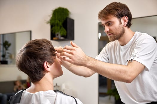 young caucasian man getting haircut by professional male hairstylist at barber shop.