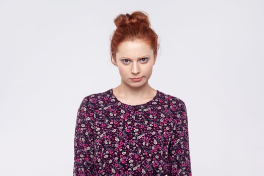 Portrait of sad upset young adult ginger woman wearing dress looking at camera with unhappy facial expression, being in bad mood. Indoor studio shot isolated on gray background.