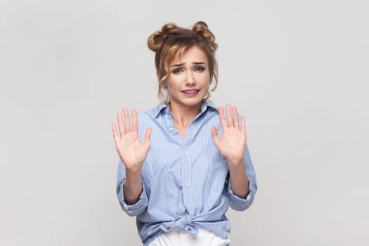 Oh no, stop it immediately. Portrait of desperate blonde woman keeps palms forward, scared of something terrible has eyes popped out, wearing blue shirt. Indoor studio shot isolated on gray background