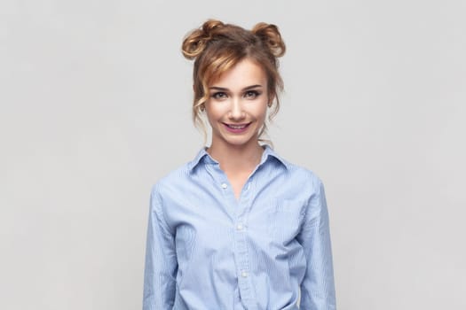 Portrait of blonde woman wearing blue shirt smiling positively after having unforgettable time with her friends, looking at camera. Indoor studio shot isolated on gray background.