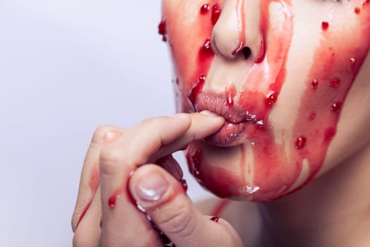 Closeup beauty portrait of attractive woman showing how the jam flowing over her face and enjoys it, keeps finger in mouth, tasting jelly. Indoor studio shot isolated on gray background.