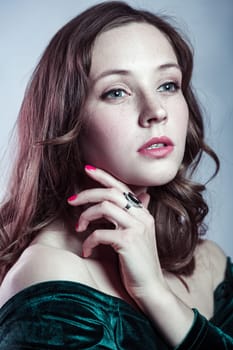 Beauty portrait of pensive attractive adorable woman with brown hair wearing green dress has red manicure, holding her chin, looking away with passion. Indoor studio shot isolated on gray background.