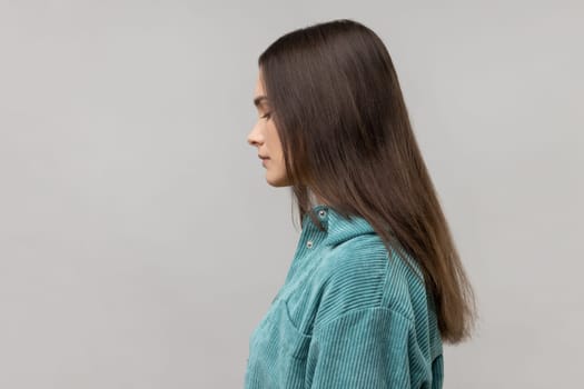 Side view of disappointed woman being upset of bad news, looking at camera with frowning face, expressing sadness, wearing casual style jacket. Indoor studio shot isolated on gray background.