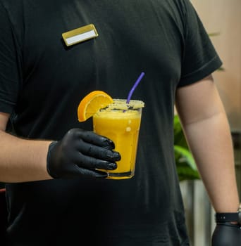 A vertical closeup of the bartender holding a glass of orange drink in the sports complex