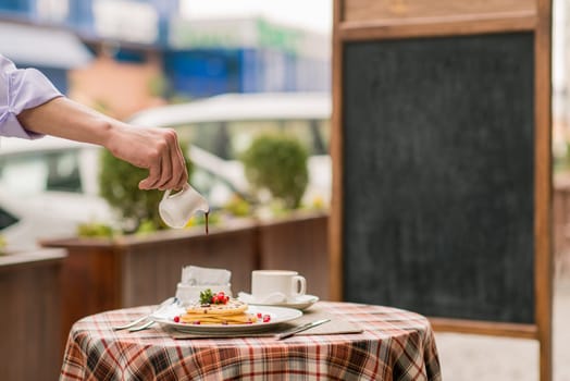 The cook pours syrup on pancakes with berries on serving table for breakfast