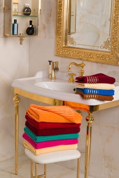 A vertical shot of folded colorful bamboo towels in a beautiful vintage golden bathroom interior