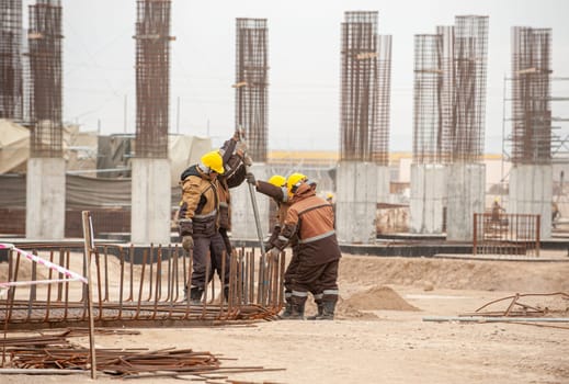 Three workers in special equipment and yellow helmets with factory construction in the background