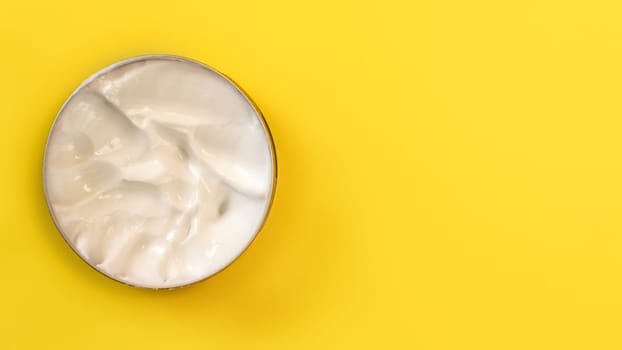 Top view - cosmetic cream in metal tin on yellow board. Space for text on the right