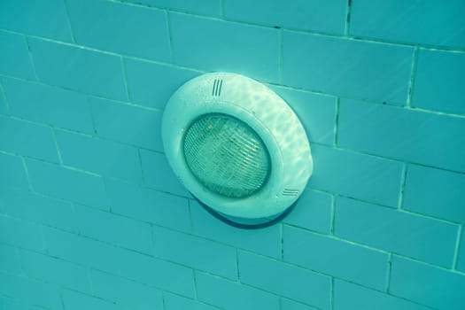 Electric light in swimming pool on blue tiles wall, sun shining from above. Underwater photo.