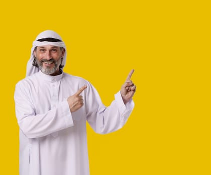 Smiling Arab man captures his cheerful and confident personalit, he points both hands towards copy space on isolated yellow background. Copy space for designers and publishers to add their text, logos. High quality photo
