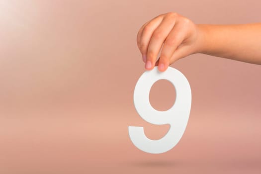 Number nine in hand. A hand holds a white number 9 on a red background. Concept with number nine. Birthday 9 years, percentage, ninth grade or day