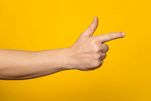 Man's hand making shooting, gesture. Hand gun gesture on isolated yellow background. Man's hand pointing a finger