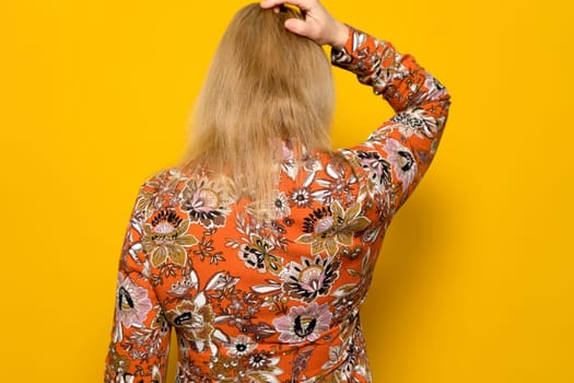 Rear view of a caucasian woman scratching her head on a yellow background. Doubt concept