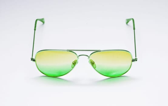 Thin-rimmed glass sunglasses with a green gradient against a white wall close-up.