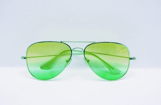 Sunglasses with a green gradient on a white wall background close-up.