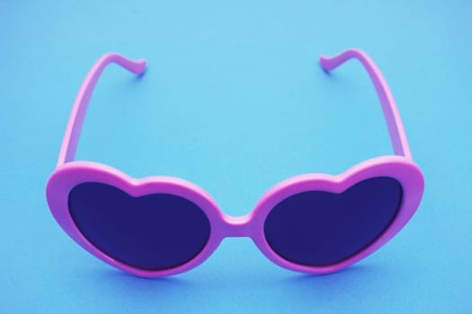 Polarized sunglasses with UV protection. Copy space. Purple heart-shaped sunglasses on a blue background...Fashionable plastic glamor women's glasses.