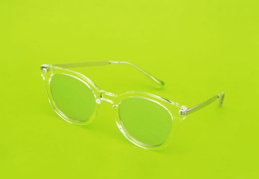 Close-up of green glasses with a transparent green frame on a rich green background.