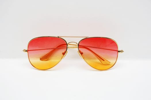 Classic thin-rimmed sunglasses with a beautiful red-yellow gradient against a white wall. Rainbow glasses with metal frames. promo or advertising banner.