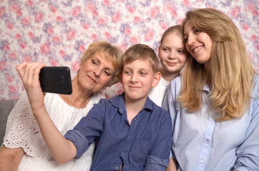 The boy takes a selfie of the family sitting on the sofa in the room.