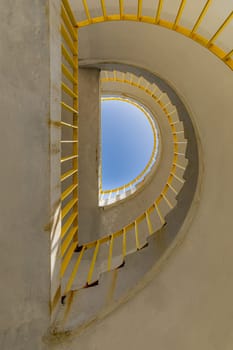 Bottom view of a concrete spiral staircase with yellow railings on a sunny morning